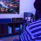 Denon AVR-S980H AV Receiver lifestyle photo of unit on cabinet under TV with person playing video games to front
