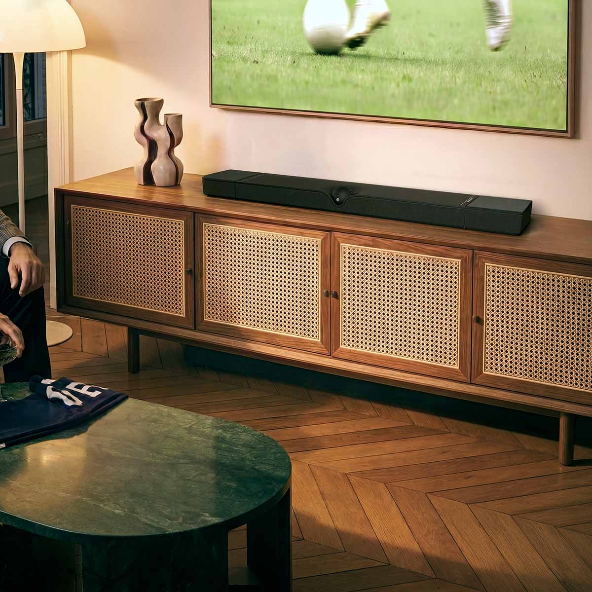 Devialet Dione Dolby Atmos Soundbar - lifestyle photo of soundbar on cabinet under TV showing soccer