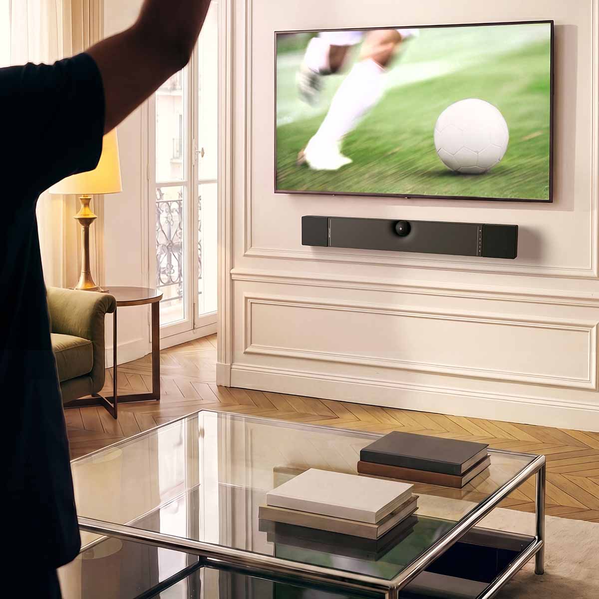 Devialet Dione Dolby Atmos Soundbar - lifestyle photo of soundbar mounted on wall under TV showing soccer