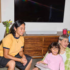 Sonos Beam Ultra Soundbar - lifestyle photo of white soundbar on a cabinet below a TV with two women and a girl in foreground