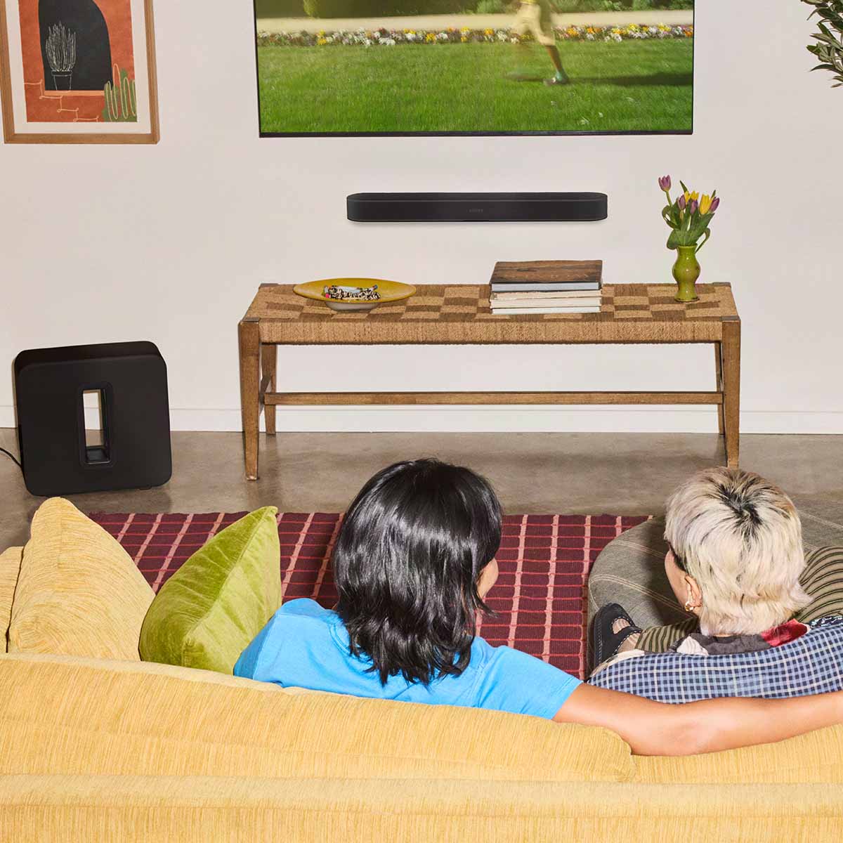 Sonos Beam Ultra Soundbar - lifestyle photo of black soundbar mounted on a wall below a TV with couple on a couch in foreground