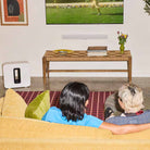 Sonos Beam Ultra Soundbar - lifestyle photo of white soundbar mounted on a wall below a TV with couple on a couch in foreground