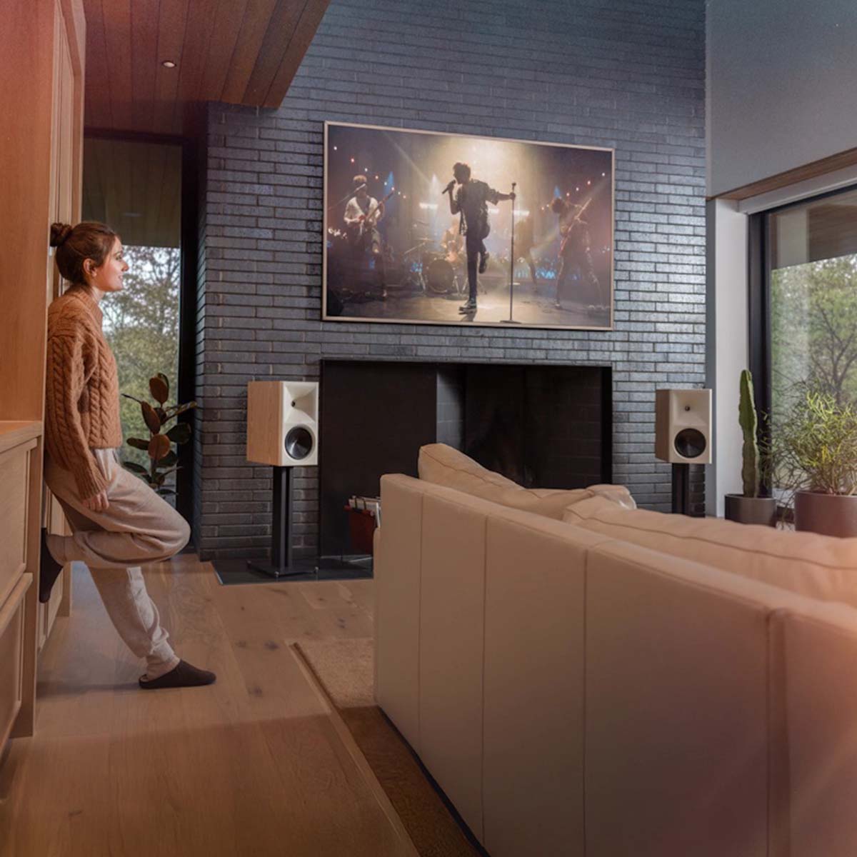 Klipsch The Nines II Dolby Atmos 8" Powered Speakers - Pair - lifestyle photo pair of speakers on stands on either side of a fireplace in a living room with woman leaning on wall to left