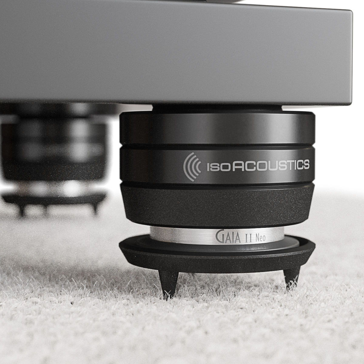 Close-up of a black IsoAcoustics GAIA Neo Carpet Disc - Black - Set of 4 on a white carpet, with another leg blurred in the background.
