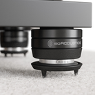 Close-up of a black IsoAcoustics GAIA Neo Carpet Disc - Black - Set of 4 on a white carpet, with another leg blurred in the background.