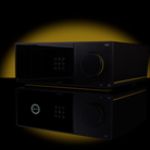 A black audio amplifier or receiver device with a glossy finish, featuring a digital keypad on the left and a large rotary volume control on the right, shown on a reflective black surface with a yellow glow behind it.