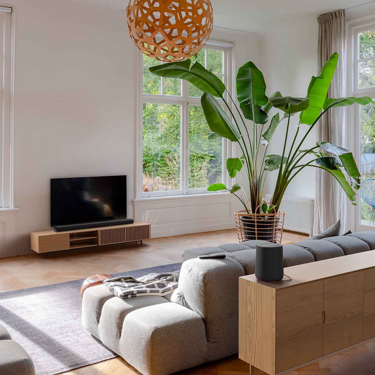 Harman Kardon Enchant 1100 Soudbar lifestyle photo with soundbar in front of TV and speaker behind couch