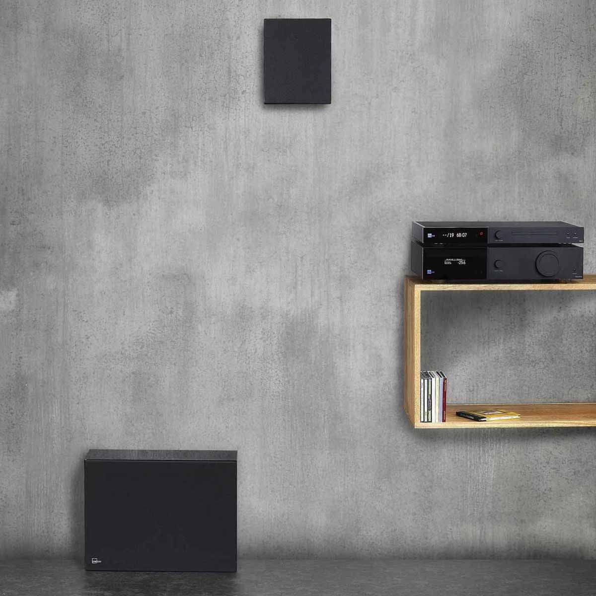 Lyngdorf BW-2 High Bandwidth Subwoofer white speaker with grille lifestyle view of speaker on floor with on-wall speaker above