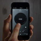 Hand holding a smartphone with Lyngdorf RoomPerfect app on a dark background