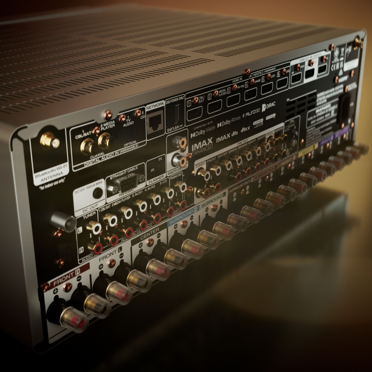 A close-up angled view of the rear panel of a large audio amplifier or receiver, showing multiple input and output jacks, switches, labels, and ports on a dark chassis.
