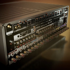 A close-up angled view of the rear panel of a large audio amplifier or receiver, showing multiple input and output jacks, switches, labels, and ports on a dark chassis.