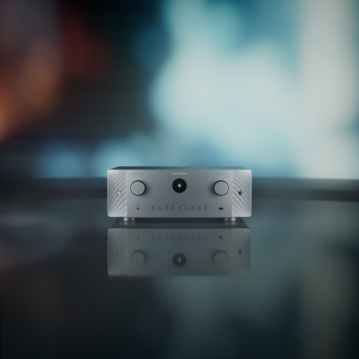 A silver Marantz Cinema 60 Series 2 AV Receiver with two front knobs and a central circular detail, displayed on a reflective dark surface against a blurred blue and black background.