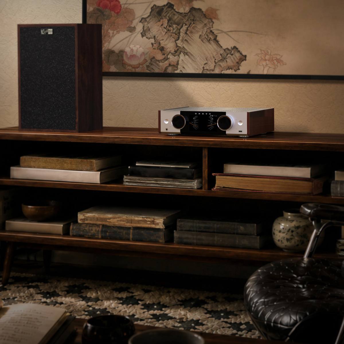 Onkyo Muse Y-50 80th Anniversary Network Streamer & Integrated Amplifier sits on a wooden media console in a styled room with books, a speaker, and a framed artwork in the background.