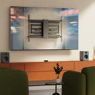 Modern living room with a large TV mounted on the wall, speakers, and a plant.