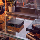 Audiolab PPA7 Phono Preamplifier - Black - lifestyle photo of unit on glass shelves to left of turntable and right of headphones on stand