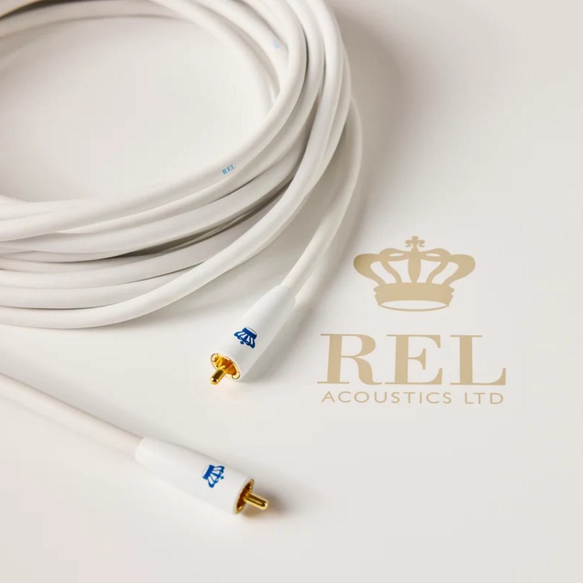 A coiled white REL Acoustics Commander .1/LFE Subwoofer Cable, displayed on a clean white background next to a gold REL Acoustics Ltd logo.