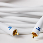 Close-up of a white REL Acoustics Commander .1/LFE Subwoofer Cable and a blue logo printed on the white sleeves, set against a soft, blurred white background.