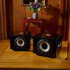 REL Acoustics S/850 Subwoofer - black - lifestyle photo of two subwoofers in front of table with flower in wood panel room no grilles
