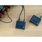 Two black SVS audio power adapters with blue LED indicators, connected to cables and placed on a light wood surface next to an audio device.