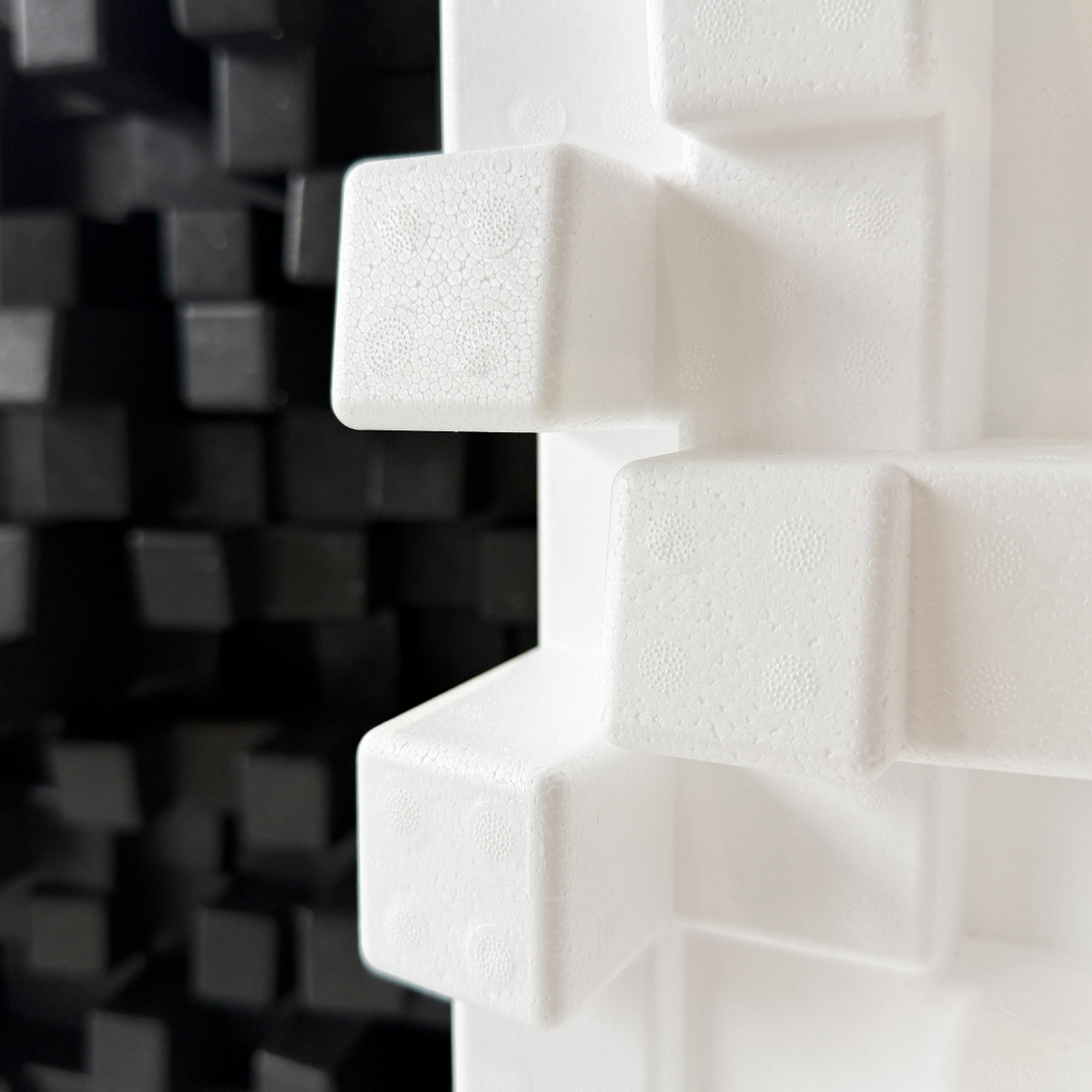 Close-up of a white Vicoustic Cinema Multifuser DC4 Acoustic Diffuser Panel with raised cube-like protrusions, shown against a blurred black foam background.