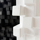 Close-up of a white Vicoustic Cinema Multifuser DC4 Acoustic Diffuser Panel with raised cube-like protrusions, shown against a blurred black foam background.
