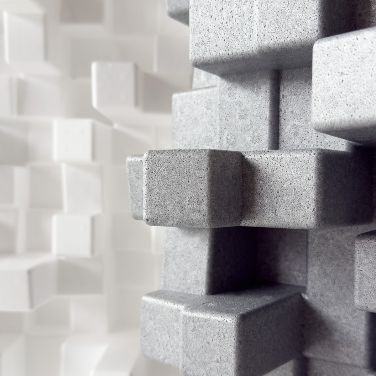 Close-up of a grey Vicoustic Cinema Multifuser DC4 Acoustic Diffuser Panel - Box of 4, with a blurred white version in the background.