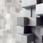 Close-up of a grey Vicoustic Cinema Multifuser DC4 Acoustic Diffuser Panel - Box of 4, with a blurred white version in the background.