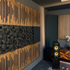 A modern room interior featuring a large wall-mounted speaker with two yellow cones, positioned in front of a dark gray cabinet. The background wall is decorated with Vicoustic Cinema Multifuser DC4 Acoustic Diffuser Panel.
