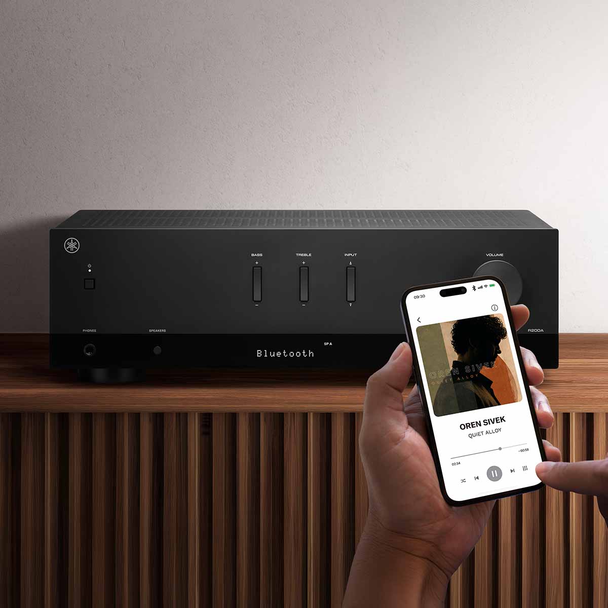 Yamaha R200A 2-Channel Hi-Fi Stereo Receiver with Bluetooth - Black - lifestyle photo of unit on cabinet with hands holding a phone selecting music in foreground