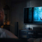 Yamaha RX500A 5.2-Channel AV Receiver - lifestyle image with dark lighting of unit on cabinet front view angled left below TV with out of focus man in foreground