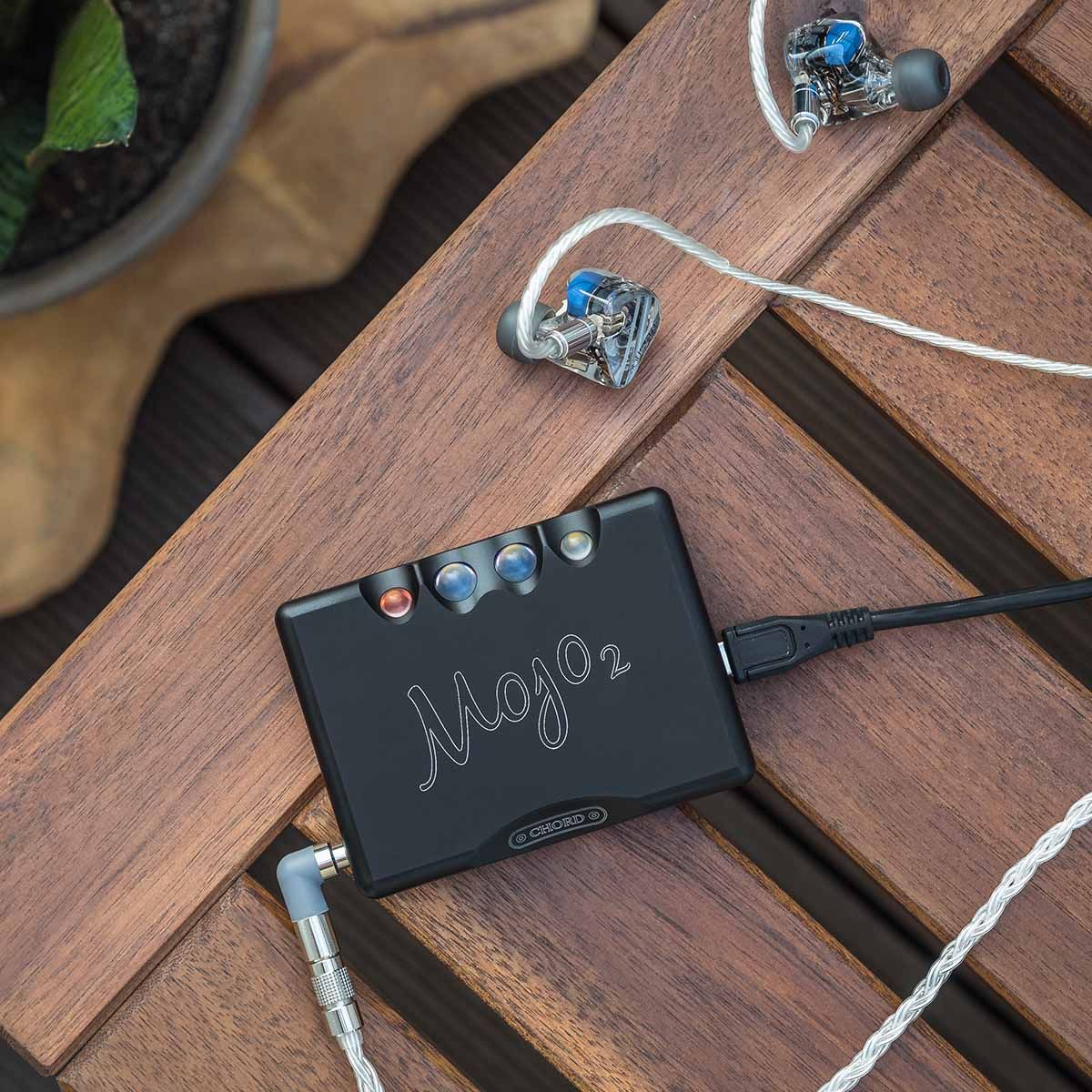Chord Mojo 2 connected to in-ear headphones sitting on outdoor table