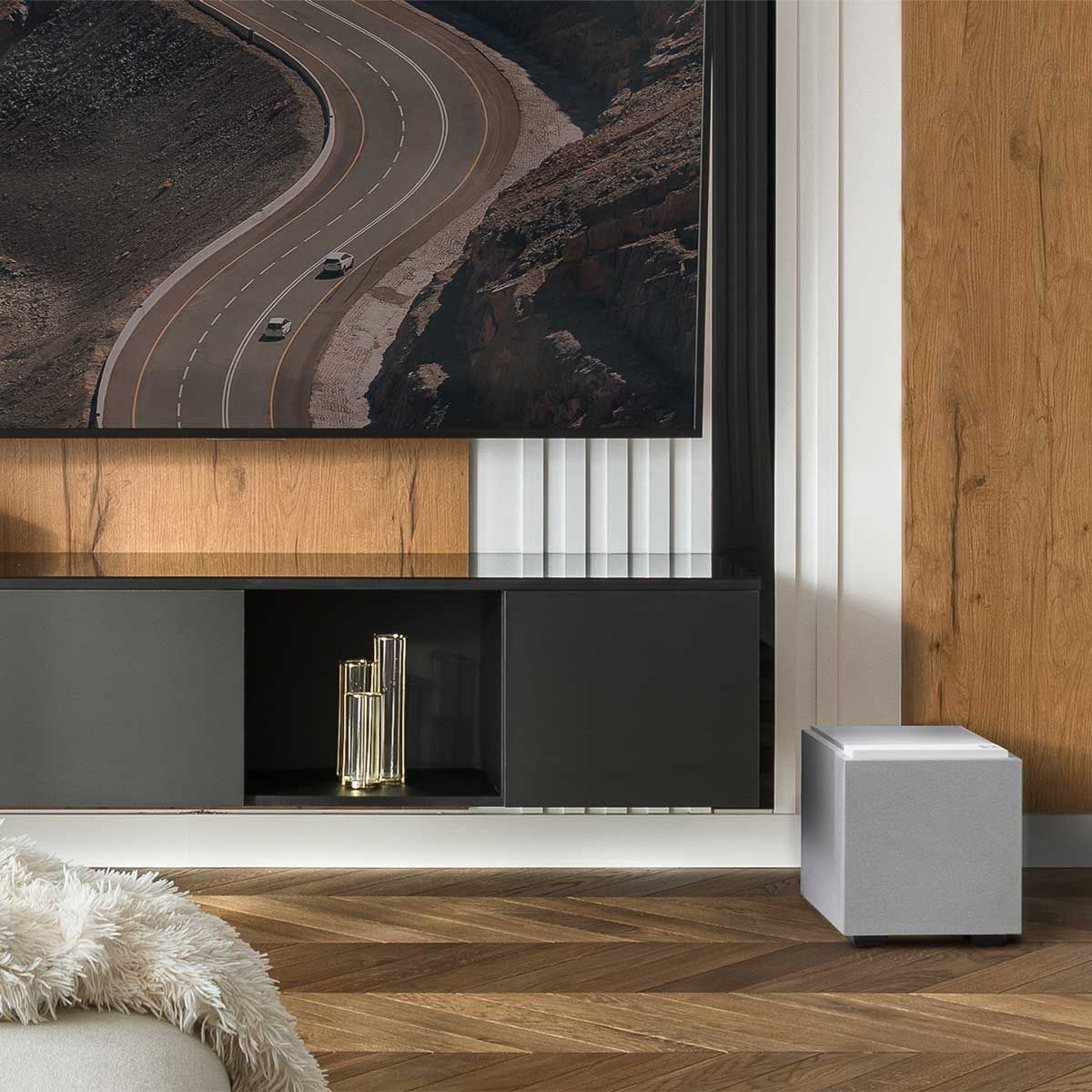 Definitive Technology Descend 8" Subwoofer, Glacier White, set up beneath a black media cabinet and a large television in a wood-paneled living space