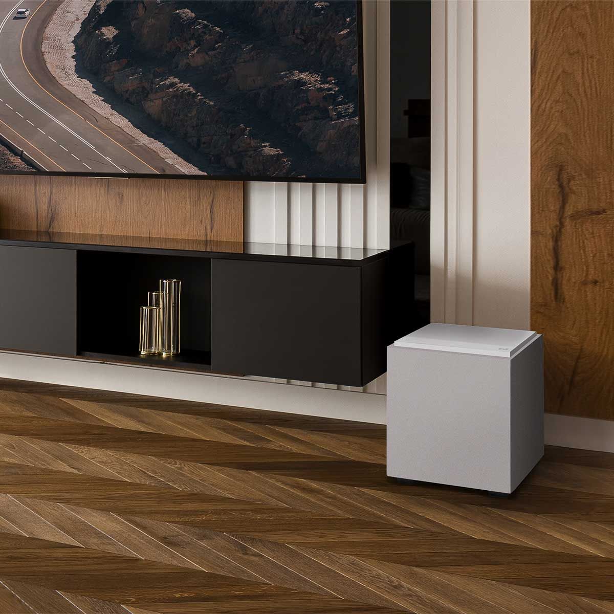 Definitive Technology Descend 8" Subwoofer, Glacier White, set up beneath a black media cabinet and a large television in a wood-paneled living space, at an angle