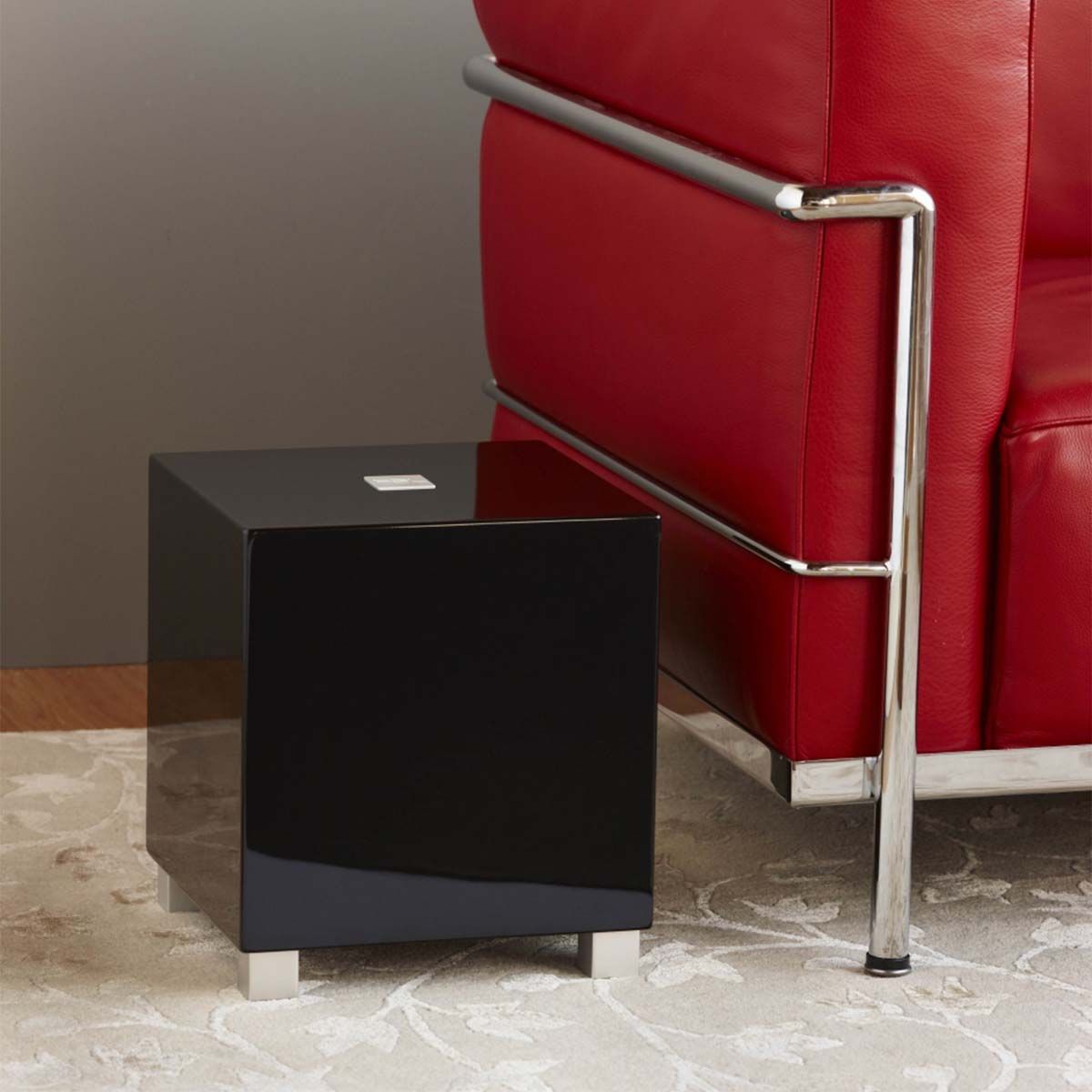 REL Acoustics Tzero MKIII Subwoofer, Black, in a living space beside a red leather couch