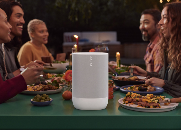 Sonos Move 2 in white at the end of an outdoor dining table surrounded by happy young adults