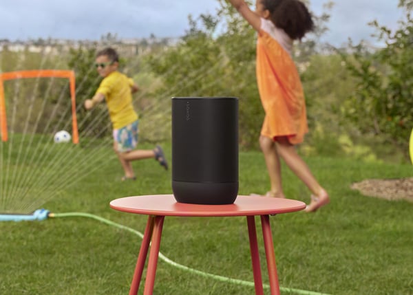 Sonos Move 2 in black outside on a red stook with children playing in a sprinkler in the background