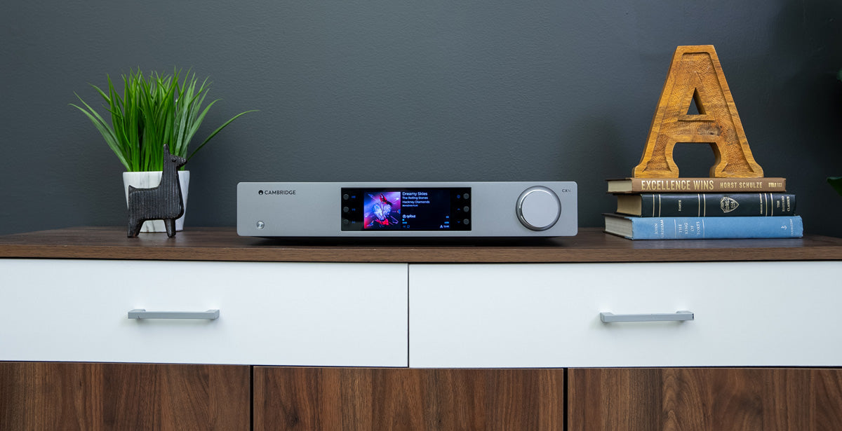 Cambridge Audio CXN100 Network Player on wooden cabinet between a plant and a stack of books
