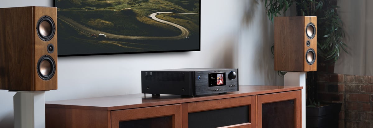 Rotel RAS-5000 Amplified Streamer in black on a console cabinet underneath a tv with speakers on either side