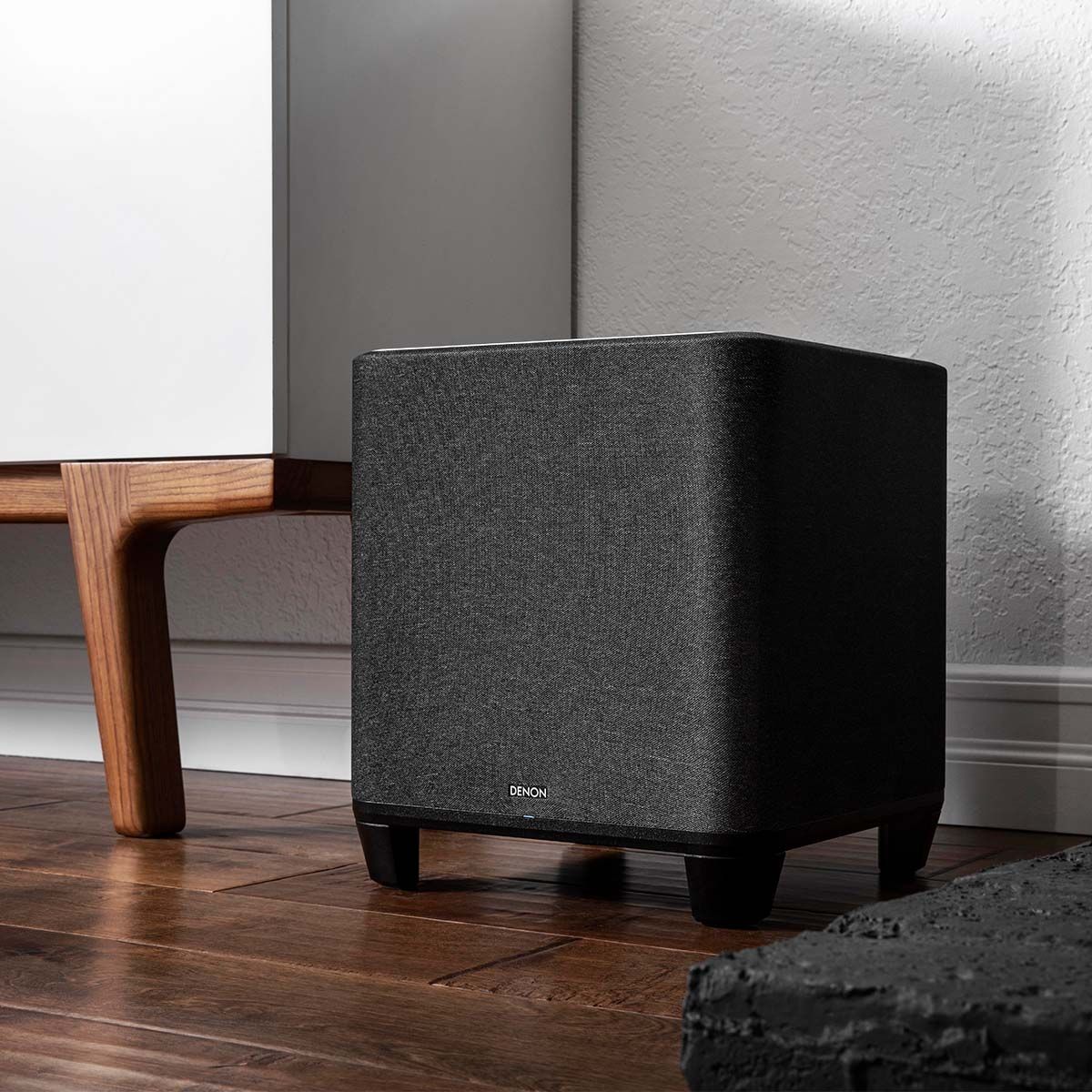 Denon Home Wireless Subwoofer, in a room beside a light wood media cabinet