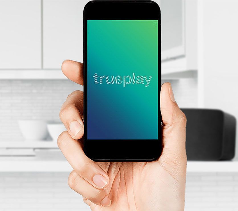 A hand model holding up a smartphone that says "trueplay" on the screen.