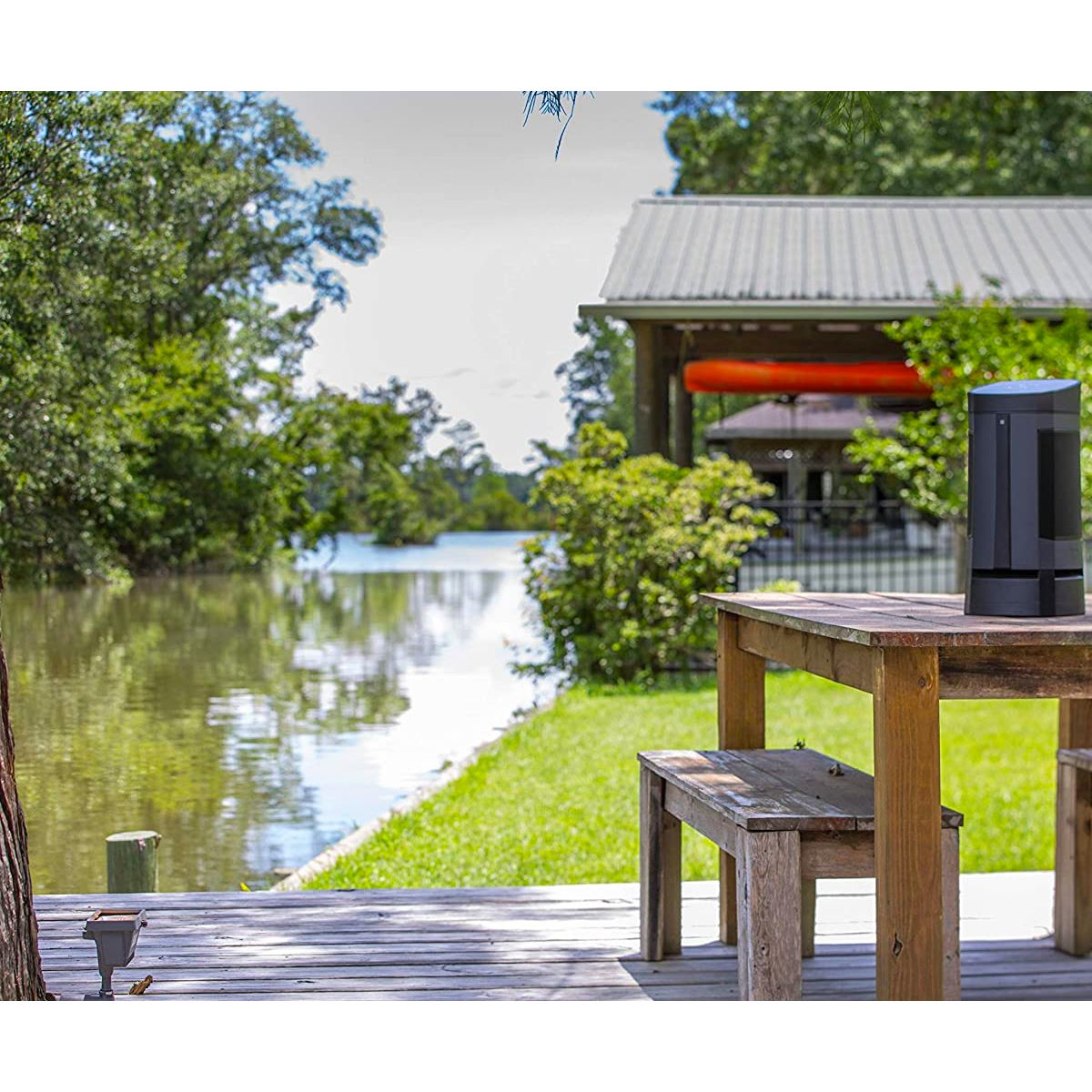 Wide-angle view of the SoundCast VG5 Bluetooth Loudspeaker on a picnic table next to a boat dock at a lake house.