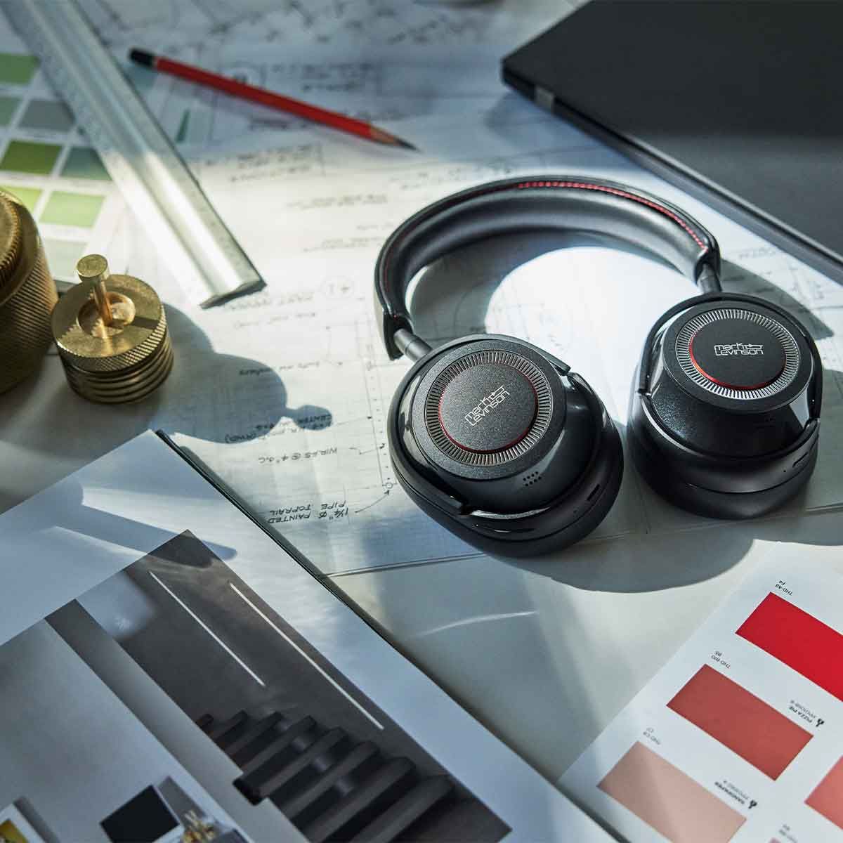 A pair of Mark Levinson № 5909 Premium Hi-Res Wireless ANC Over-Ear headphones laying on a work desk with papers and rulers spread out on the table.
