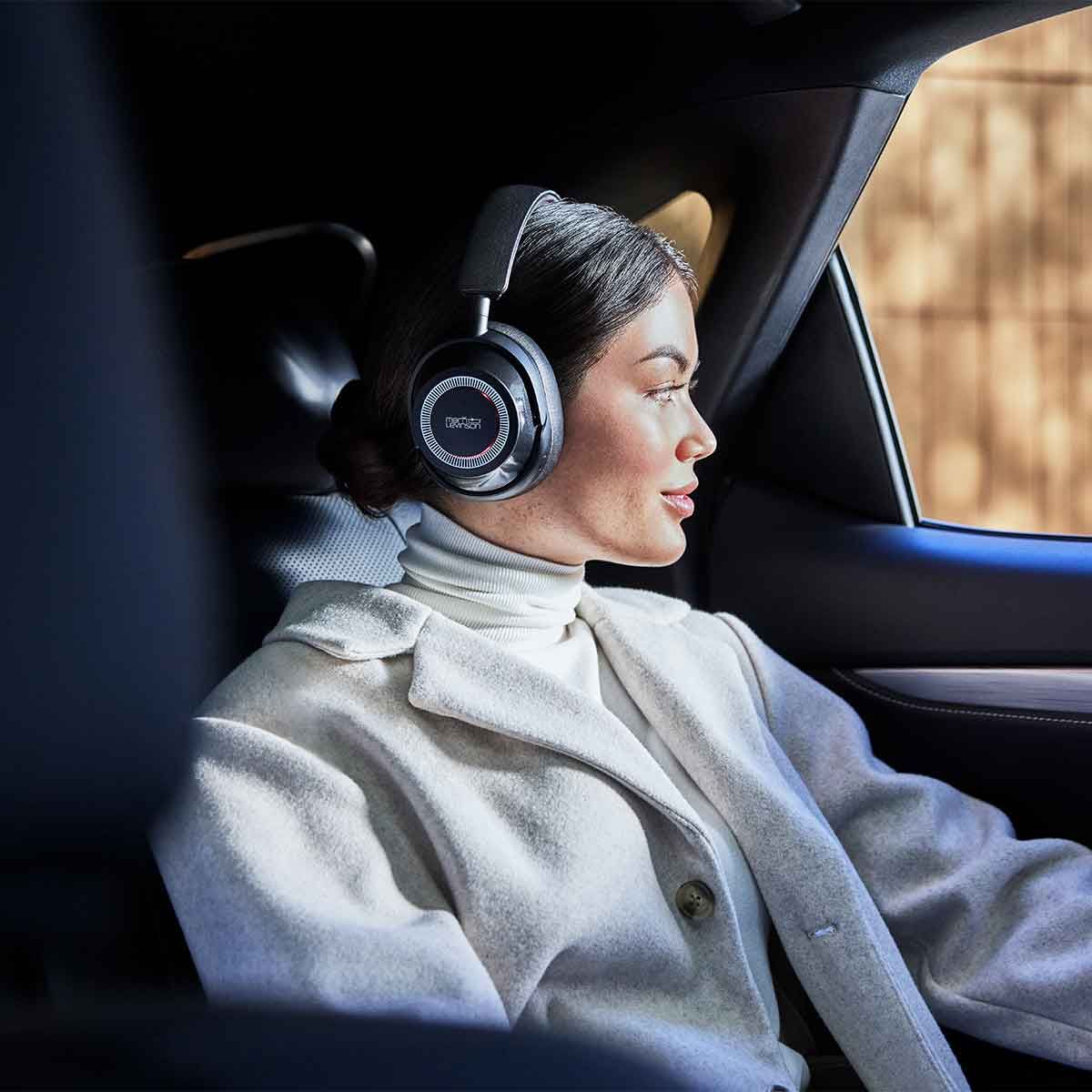Female model wearing a pair of Mark Levinson № 5909 Premium Hi-Res Wireless ANC Over-Ear headphones in the pewter finish while riding passenger inside of a vehicle.