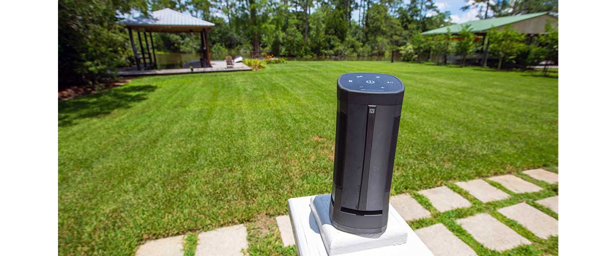 Close up of Soundcast VG5 Portable Waterproof Bluetooth Speaker streaming audio on the lawn in the backyard on a sunny day