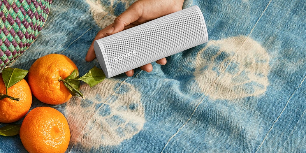 Sonos Roam Portable Speaker, at a picnic with some oranges and a human hand