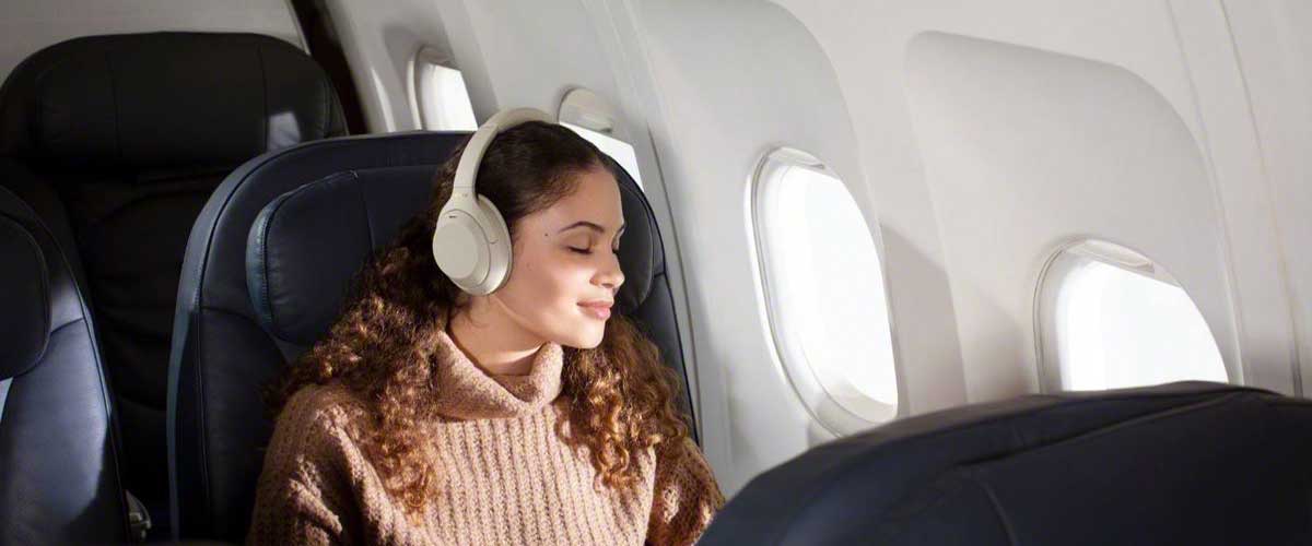 female model wearing a pair on Sony WH1000XM4 noise cancelling headphones on an airplane