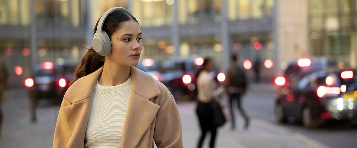 woman walking in the street wearing a pair of Sony WH-1000XM4 noise cancelling headphones