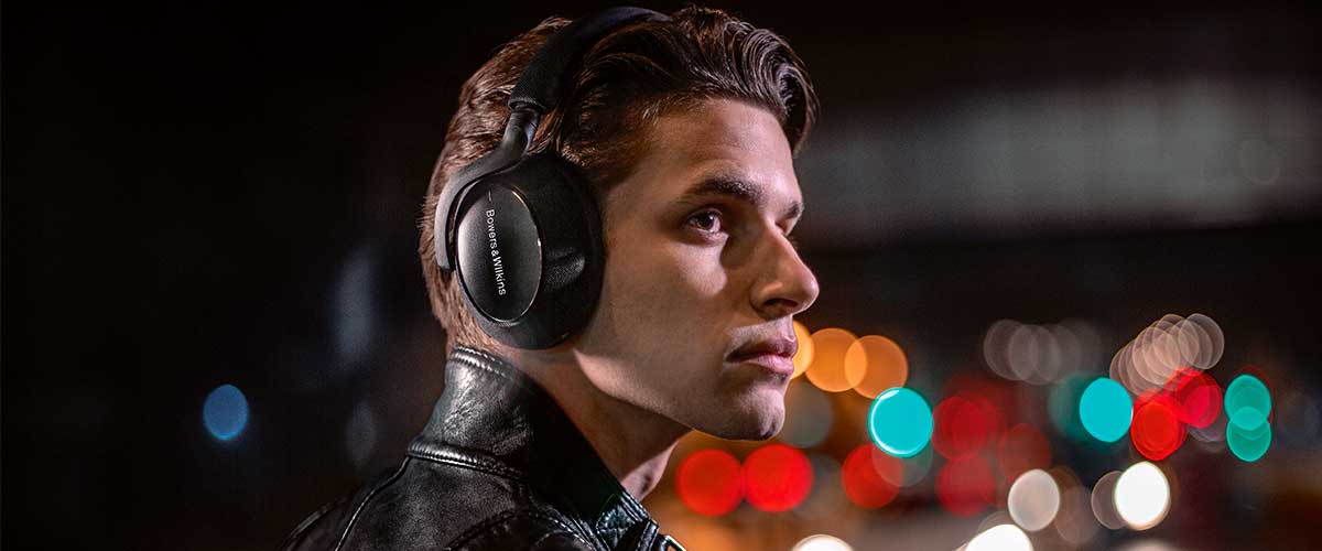male model wearing a pair of Bowers and Wilkins PX7 Carbon Edition noise cancelling headphones in a busy street at night
