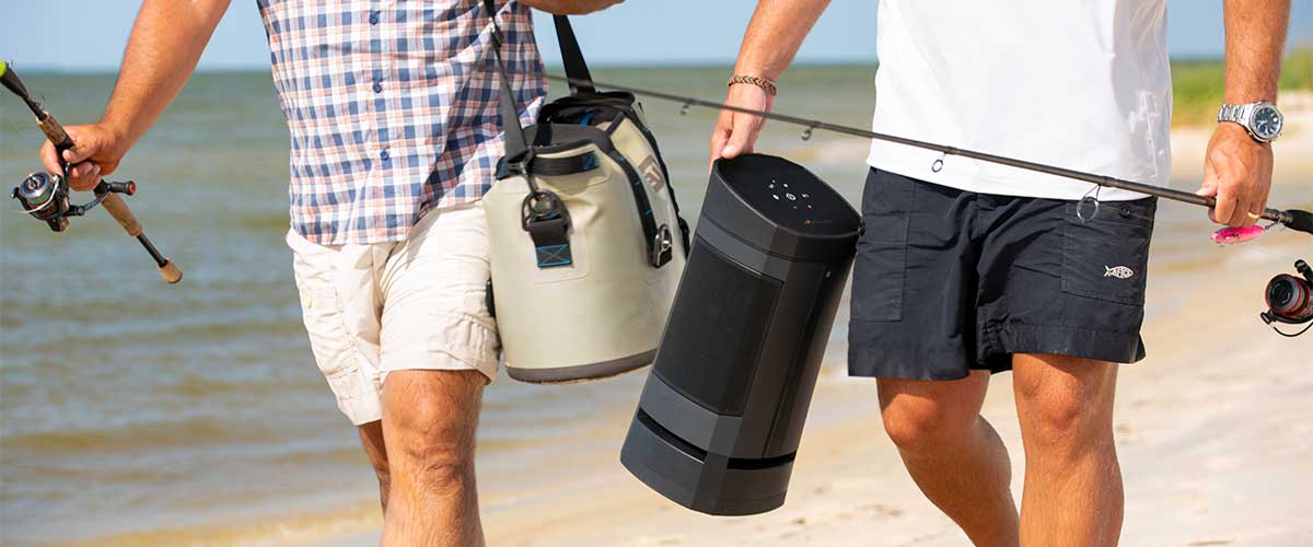 two male models carrying fishing poles and the VG5 portable bluetooth speaker while on the beach 