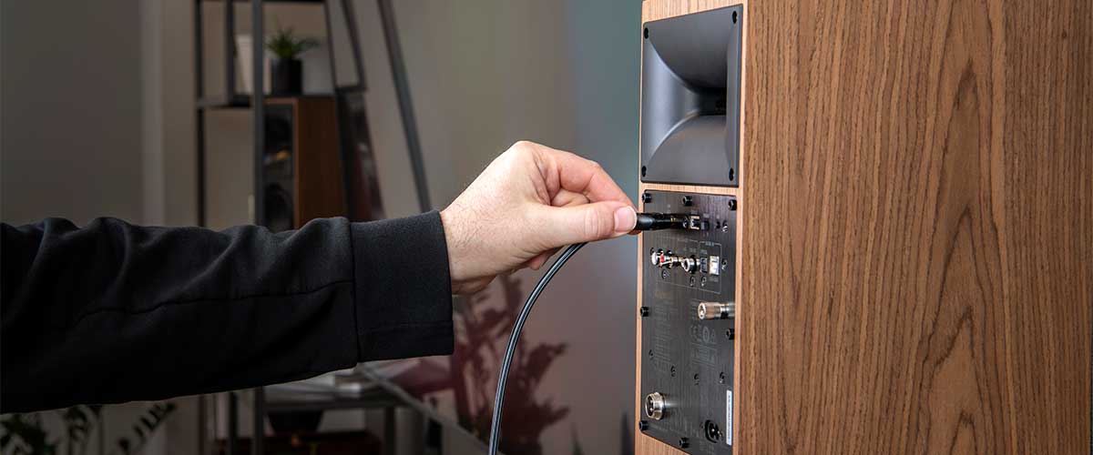 close up shot of a hand model connecting an audio cable into the Klipsch The Fives Powered Speaker System.